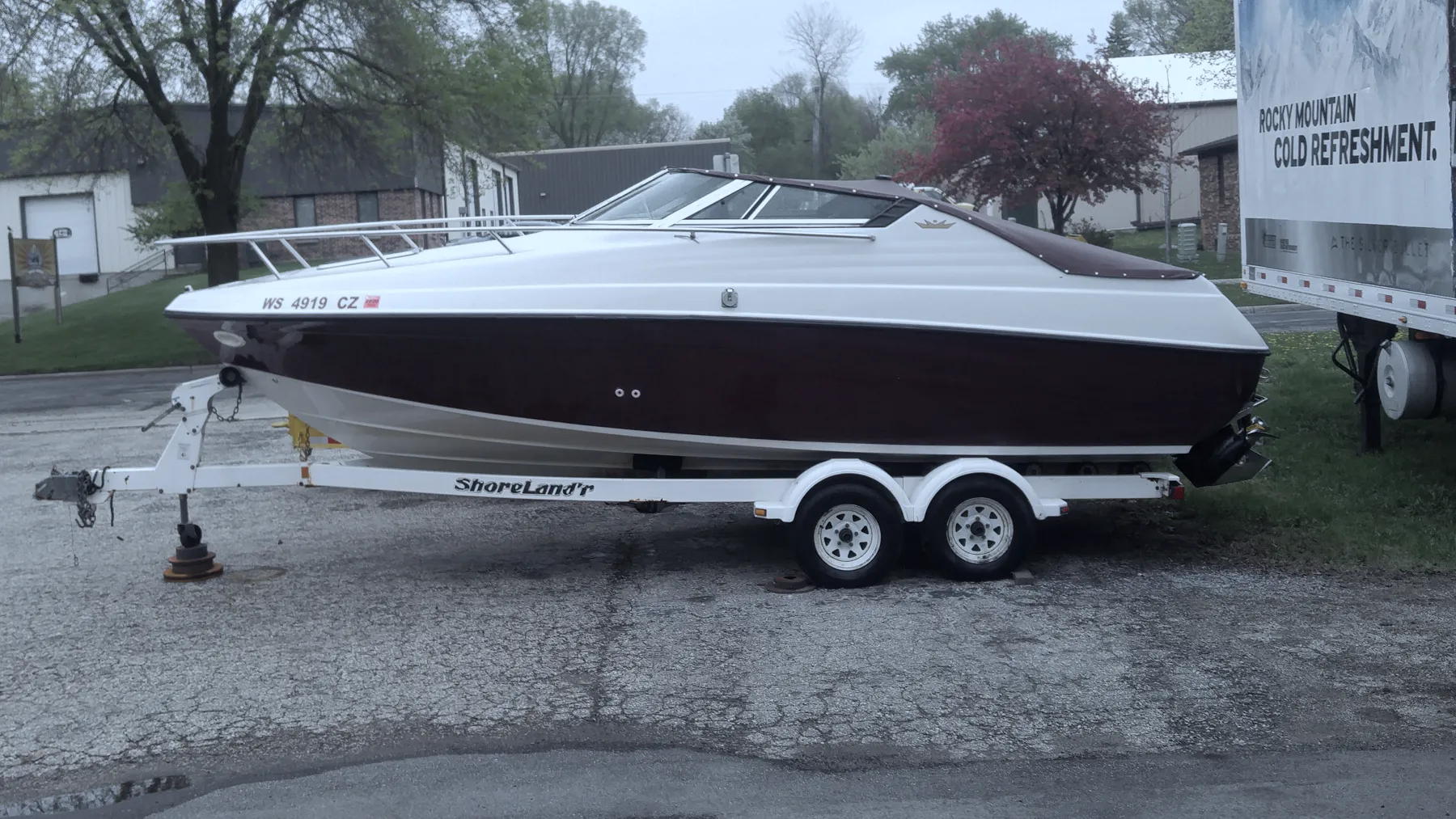 White and burgundy boat on a trailer outside the building